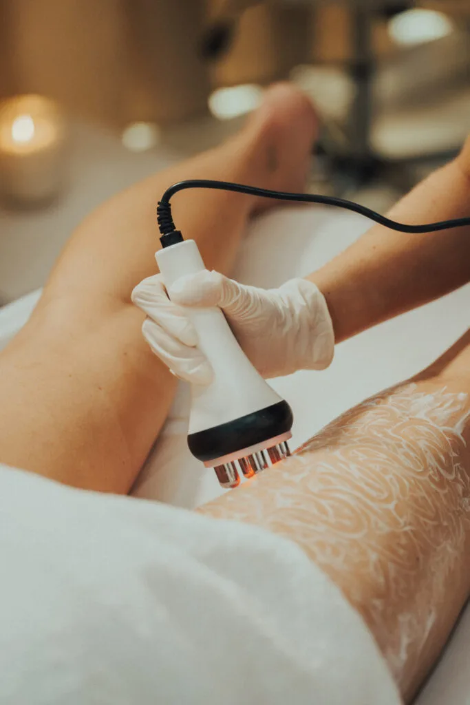 A therapist applying a body-treatment handset to a client's thigh