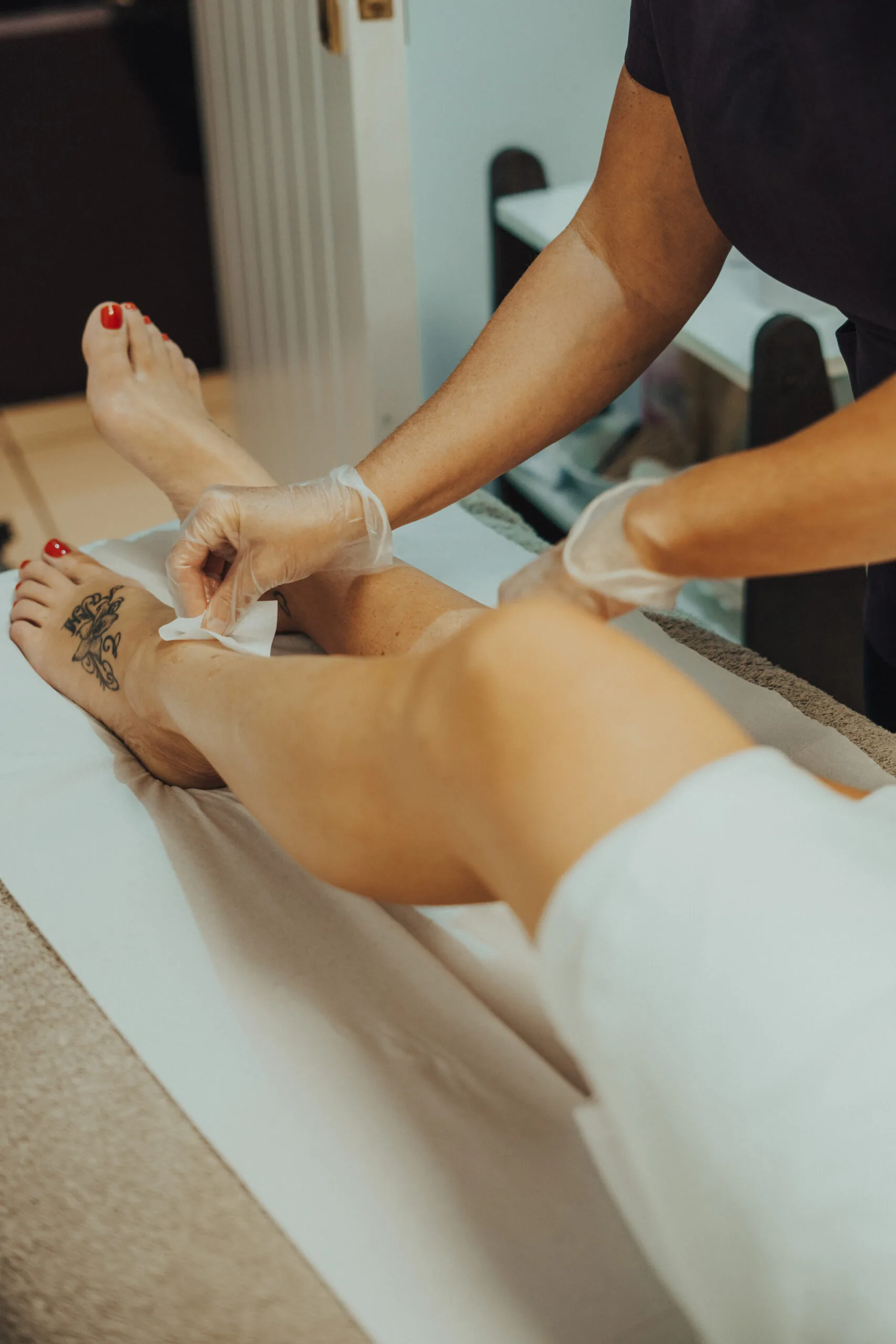 A therapist using a waxing strip on a client’s lower leg