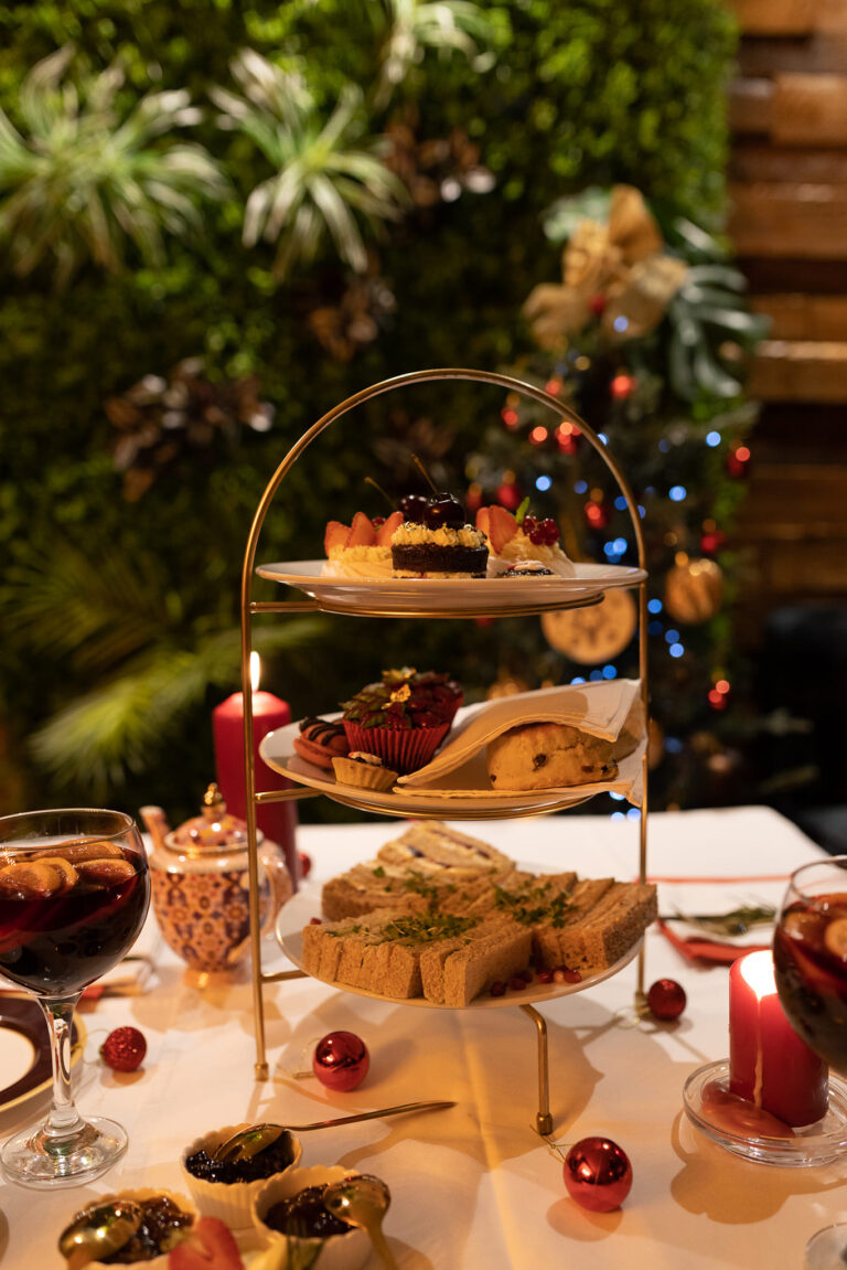Three-tier afternoon tea with sandwiches and sweet treats on a candlelit festive table